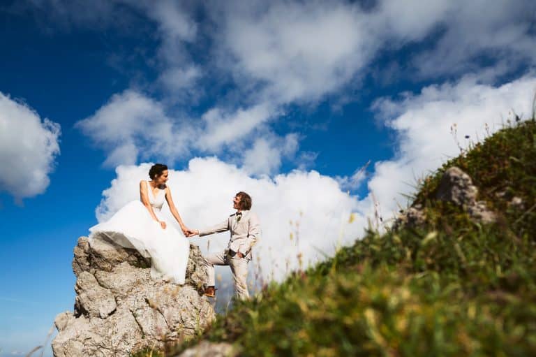 Newlyweds in the mountains looking each other while bride is sitting on the rock